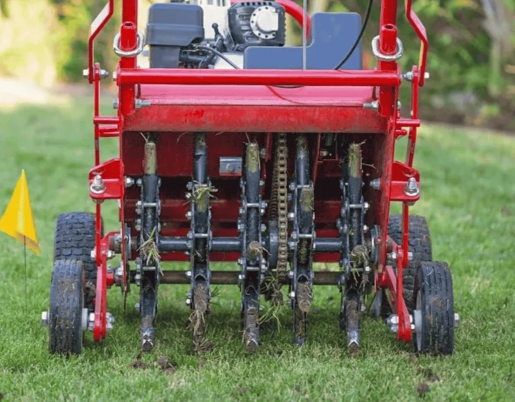 Rear view of a core-aerator machine puncturing lawn soil, removing small plugs for improved root growth.