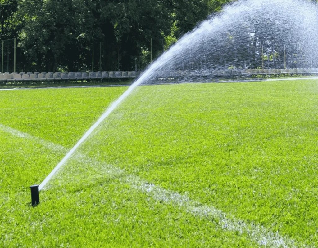 Fine mist of liquid aerator solution dispersing over a well-kept sports field to improve soil health.